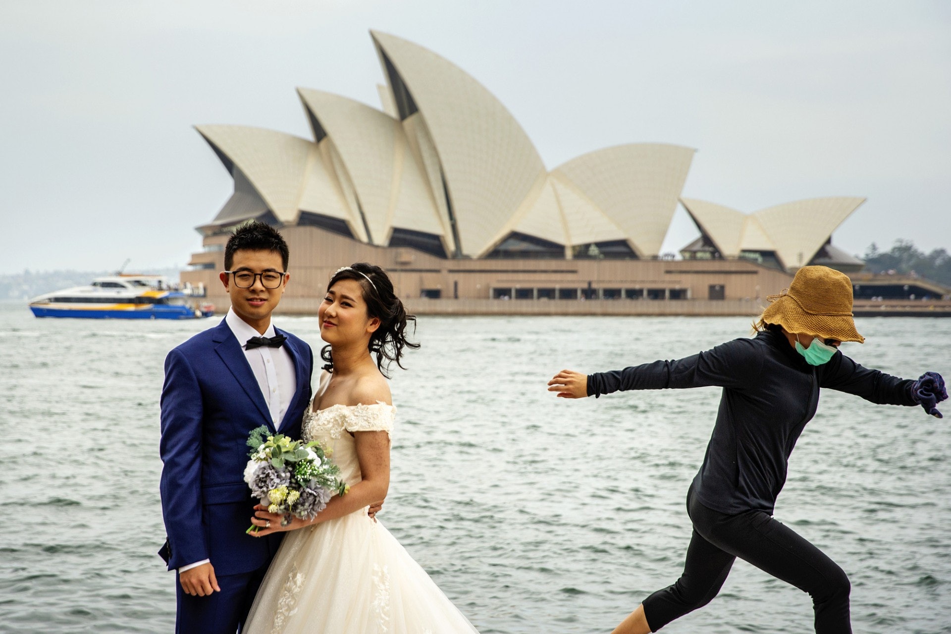 2020年1月29日，一對新人在悉尼灣拍攝婚照，一名戴口罩的女子從旁跳開。（Jenny Evans／Getty Images）