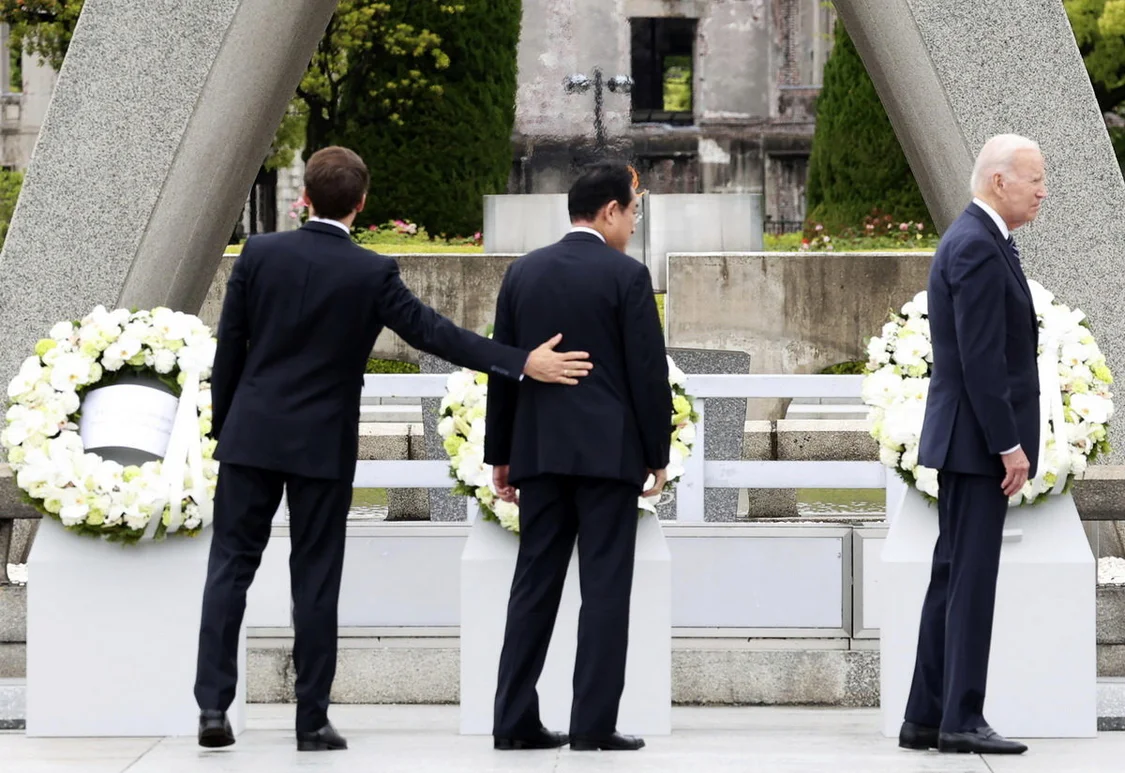 当地时间5月19日，日本广岛，七国集团峰会开幕，在广岛和平纪念公园，法国总统马克龙在悼念原子弹爆炸受害者纪念碑前祈祷后，把手放在日本首相岸田文雄的背上，右边为美国总统拜登。